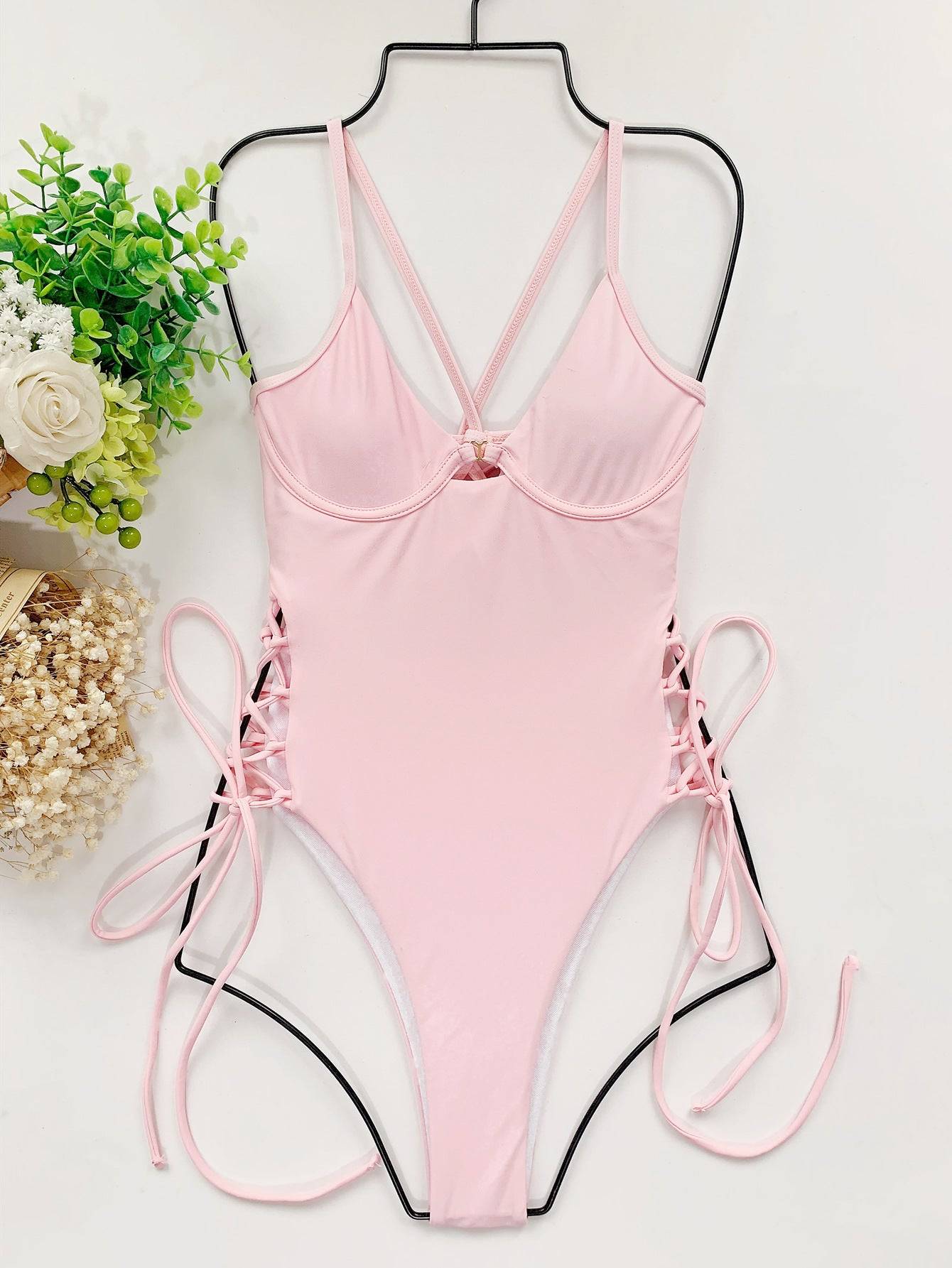 Цял бански ''Pink Angora'' в розово, изложен на закачалка, показващ детайлите на дизайна и връзките отстрани.
